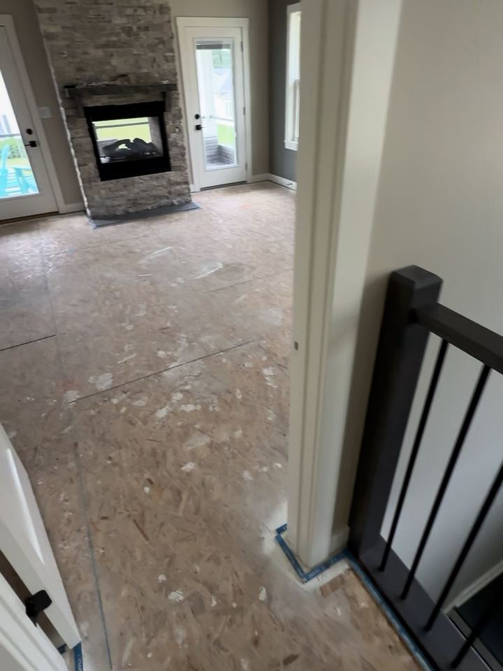 Before: bare OSB subfloor in a new-construction primary bedroom with a stone fireplace, Cicero